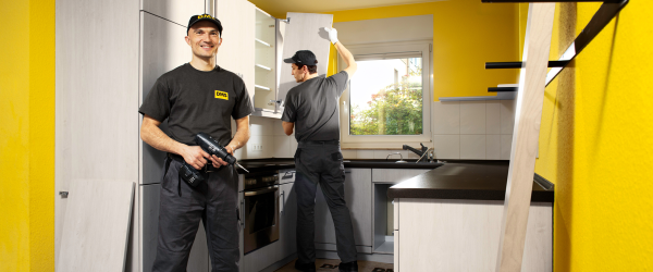 Zwei Servicemonteure der DMS montieren eine Einbauküche in einem gelb gestrichenen Raum.