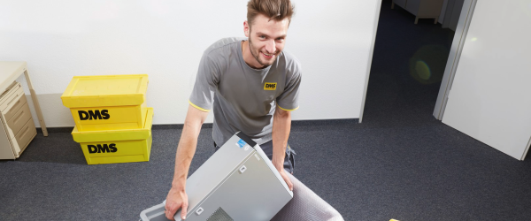Lächelnder junger Mann, der einen Computer in eine Box packt.