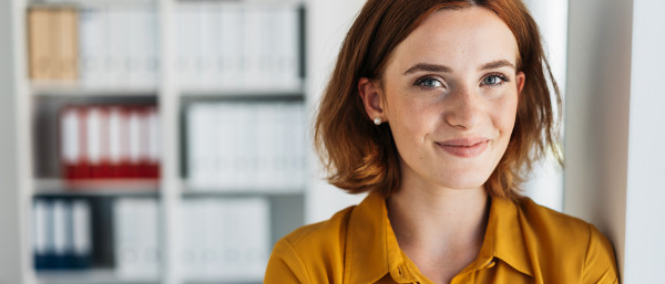 Freundliche Frau im Büro lächelt in die Kamera; daneben Hinweise auf unbefristete Stelle, Wechselprämie (1.200 €) und 13. Gehalt sowie Kununu-Siegel „Top Company 2024“.