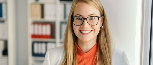 Mitarbeiterin im Personalwesen in moderner Büro­umgebung mit Aktenregalen im Hintergrund.