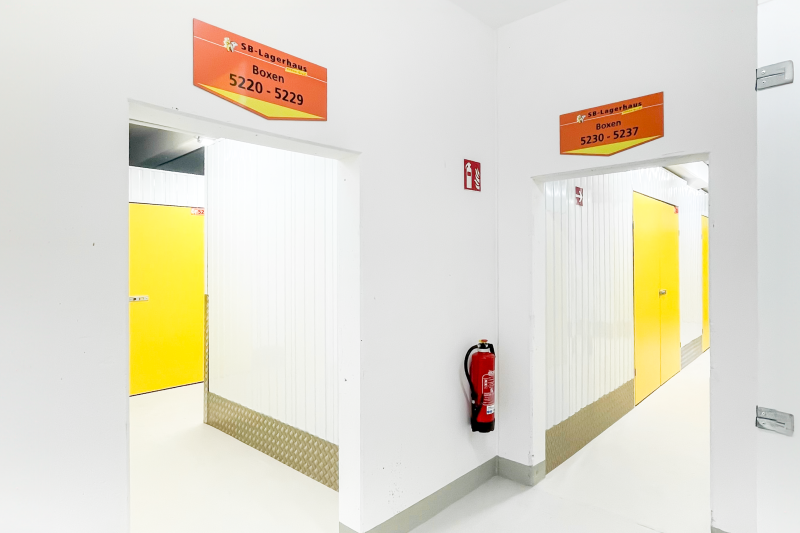 Innenbereich eines Self-Storage-Lagers mit gelben Türen, Beschilderung und Feuerlöscher an der Wand.
