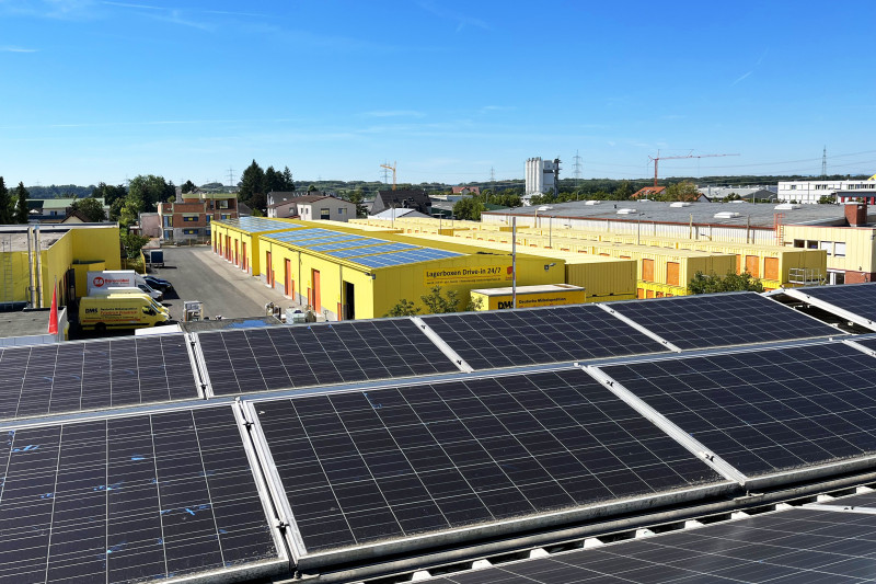 Solaranlagen auf Dächern von gelben Lagerhallen in einem Gewerbegebiet bei sonnigem Wetter.