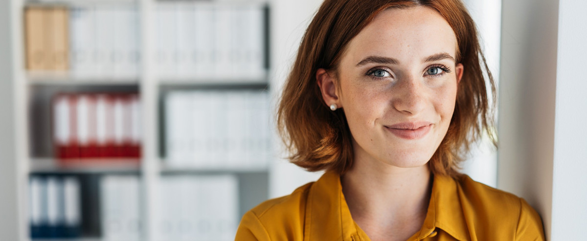 Auszubildende in der Marketingkommunikation in moderner Büro­umgebung vor einem Regal mit Aktenordnern.