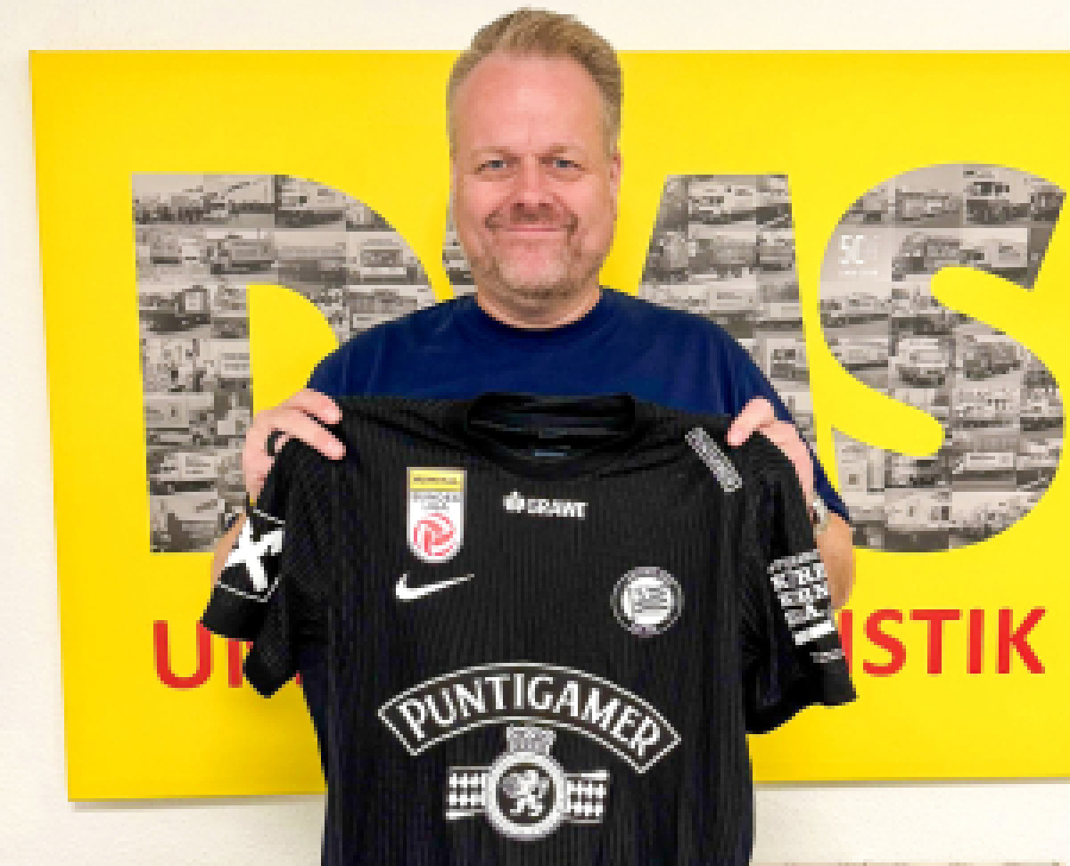 Mann hält Fußballtrikot in der Hand und lächelt