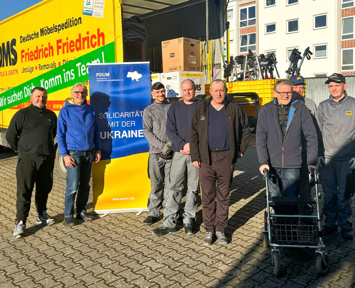 Gruppe von Männern vor einem Spenden-Lkw mit DMS-Logo und Banner „Solidarität mit der Ukraine“.