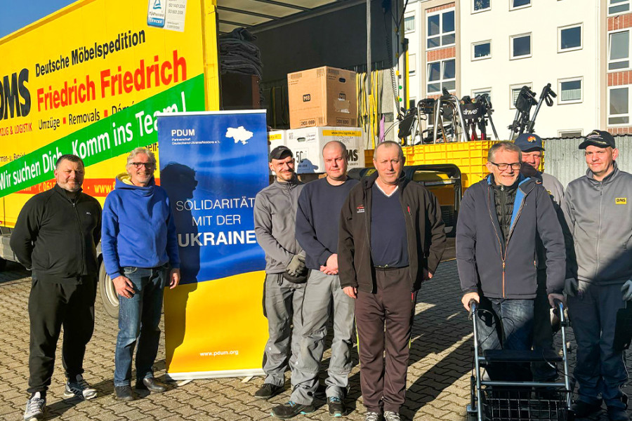 Gruppe von Männern vor einem Spenden-Lkw mit DMS-Logo und Banner „Solidarität mit der Ukraine“.