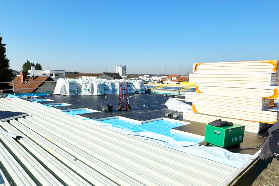 Dachsanierung mit Dämmmaterial und Bauelementen auf einem Flachdach bei sonnigem Wetter.