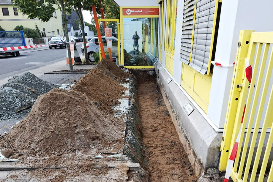 Baustelle vor dem Eingang von KS Büromöbel mit ausgehobenem Graben und Erdhaufen entlang der Fassade.